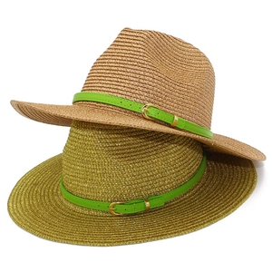 Detail of woven straw sun hat with glossy texture and green leather band with metal buckle