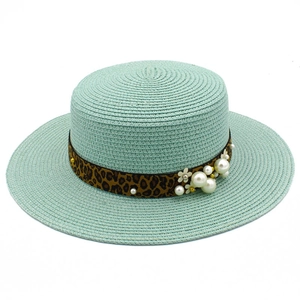 Close-up of mint green straw hat with leopard ribbon, pearls, and flower details