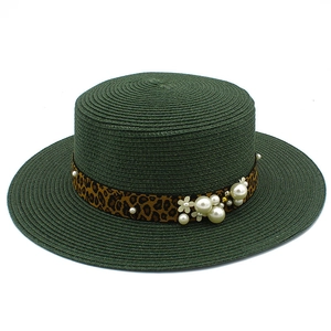 Detail of dark green straw hat with leopard ribbon, pearls, and floral embellishments