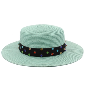 Détail d'un chapeau de paille vert menthe avec strass colorés sur le ruban noir décoratif