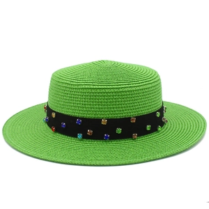 Gros plan détaillé du chapeau de paille vert vif avec des strass colorés sur ruban noir