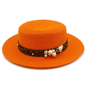 Detail of orange woven straw hat with leopard print band and pearl floral accents