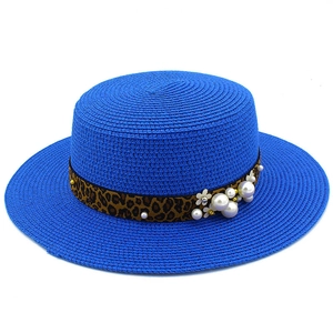 Close-up of blue boater straw hat featuring leopard print ribbon and pearl floral details