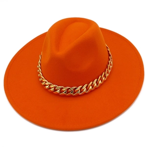 Détail d'un chapeau fedora orange vif avec une grosse chaîne en métal doré sur le bord