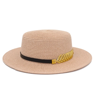 Detailed macro view of beige straw hat featuring black band and golden leaf metal ornament