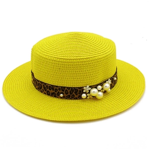 Detail of yellow straw boater hat featuring leopard ribbon, pearls and floral accents