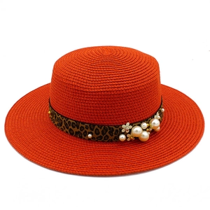 Detail of orange straw hat with leopard print band, pearls, and white floral accents