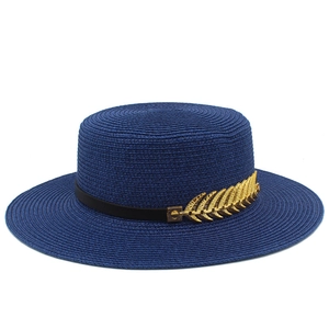 Close-up of a navy boater hat with fine woven texture and a gold leaf metal ornament