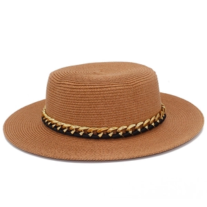 Détail d'un chapeau de paille à bord plat avec une chaîne dorée élégante et texture tressée