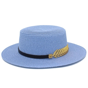 Detail of the blue boater straw hat featuring a black ribbon and gold leaf metal accessory