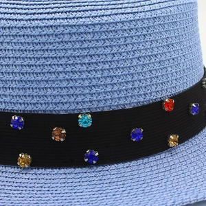 Détail d'un chapeau de paille bleu clair avec strass colorés sur un ruban noir