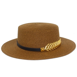 Detail of a brown woven straw boater hat with black band and gold leaf metal accessory