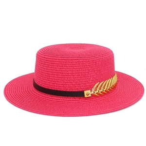 Detail of fuchsia straw boater hat featuring a black leather band and gold leaf ornament
