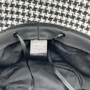 Detail view of cotton houndstooth bucket hat interior with adjustable strap and care label