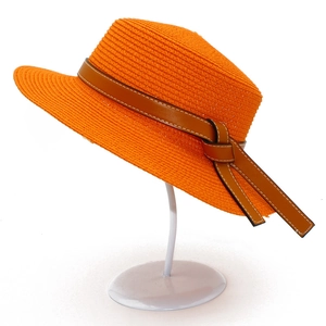Detailed macro view of bright orange straw hat featuring a brown leather bow and white stitching