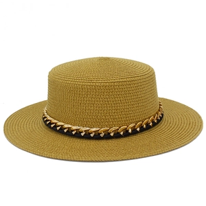 Détail de la texture d'un chapeau de paille à bord plat avec chaîne dorée et ruban noir