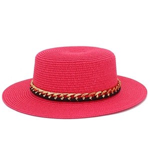 Détail d'un chapeau canotier fuchsia avec chaîne en métal doré et ruban tissé noir