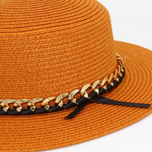 Détail d'un chapeau de paille orange avec chaîne dorée et ruban noir élégant