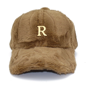 Detalle de gorra de béisbol de felpa camel con emblema metálico R en color dorado