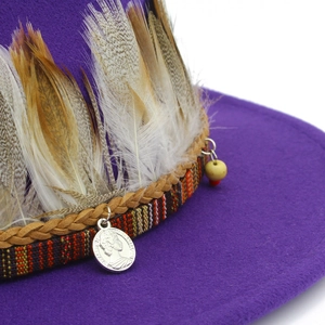 Detail of purple fedora hat featuring ethnic ribbon, feathers, and silver coin pendant