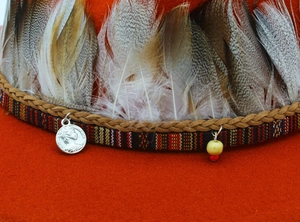 Detail of warm orange felt fedora featuring ethnic woven band with feathers and coin pendant