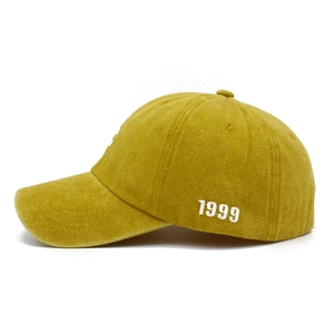 Detail view of mustard yellow cotton baseball cap with white 1999 embroidery on side