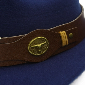 Dettaglio cappello cowboy in feltro blu con cinturino in pelle e decorazione testa di toro