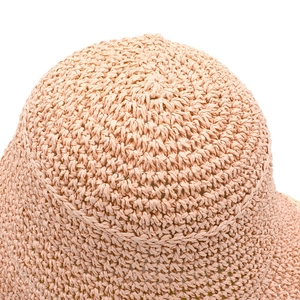 Dettaglio ravvicinato della trama in paglia intrecciata di un cappello estivo rosa pesca