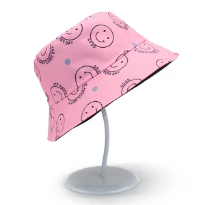 Détail d'un chapeau bob rose avec motifs smileys sur un support en métal minimaliste