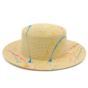 Close-up of beige straw hat with vibrant blue and pink paint splatter detail