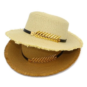 Detail of straw hat featuring raw fringe edge and gold leaf metal accessory on leather band