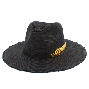 Detailed macro view of black woven straw hat with golden leaf metal trim and frayed edges