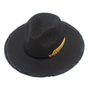 Detailed close-up of a black straw fedora with a golden leaf metal accent on the band
