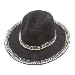 Detail of woven straw hat featuring dual-row pearls and metallic cone studs on brim