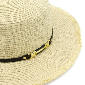 Dettaglio cappello di paglia beige con bordo sfrangiato, fascia nera e fibbia d'oro