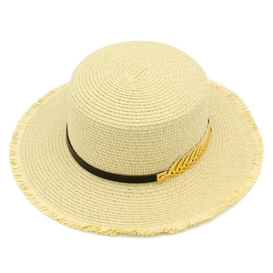 Close-up of woven straw hat featuring black ribbon, golden leaf charm, and frayed edges