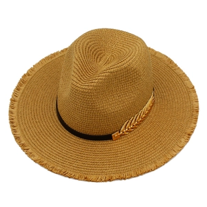 Close-up of beach straw hat featuring a golden leaf charm and black decorative band