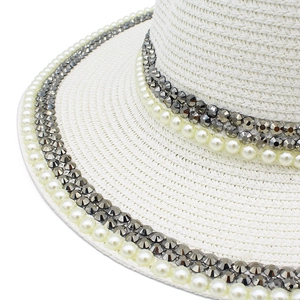 Detail of white woven straw hat featuring elegant faux pearls and grey rhinestone bands