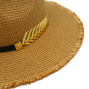 Close-up of woven straw sun hat featuring a gold leaf accessory and frayed edge detail