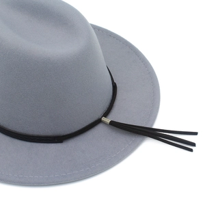 Detail view of a light gray wool felt fedora featuring black band and leather tassels