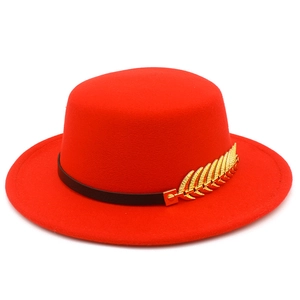Detail of red flat top felt hat featuring a black leather band and gold feather ornament