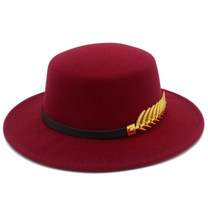 Detail of burgundy flat top fedora hat with gold feather metal pin and black leather band