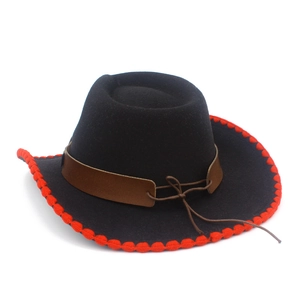 Detail of black cowboy hat featuring decorative red pom-pom trim and brown leather band