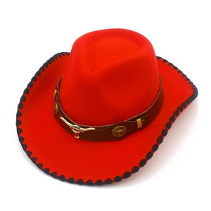 Macro detail of red felt cowboy hat featuring a golden bull head ornament and black stitched edge