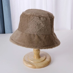 Close-up detail of plush brown bucket hat showing soft faux fur texture on a wooden stand