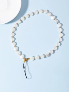 Détail des perles de coquillage blanc et perles dorées sur une dragonne de téléphone