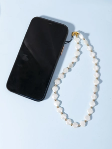 Détail de perles en forme de coquillage et accents dorés sur un bijou de téléphone