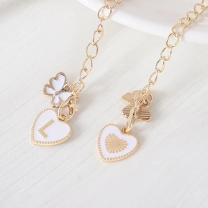Macro shot of gold cup chains with white enamel heart letter L and butterfly charm detail
