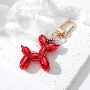 Vibrant red resin balloon dog keychain with polished gold hardware on a textured stone base