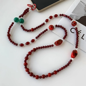 Détail d'une chaîne de téléphone en perles acryliques rouges et vertes avec breloques